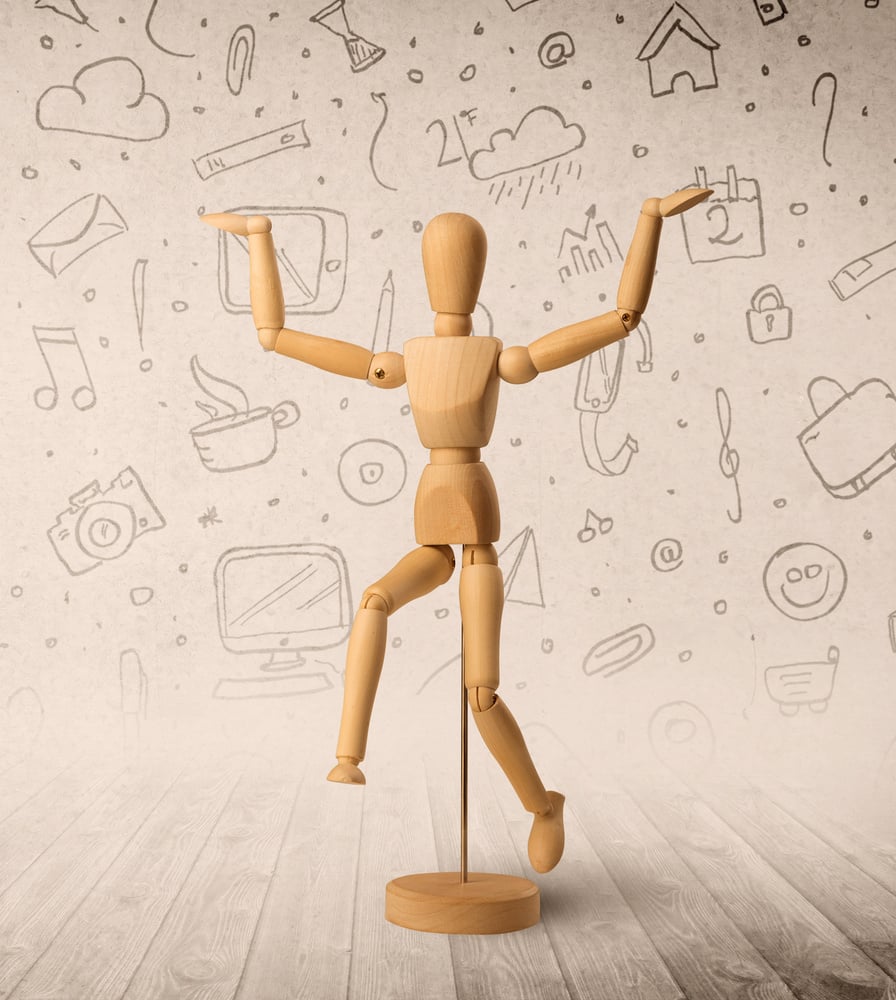 Wooden mannequin posed in front of a greyish background with mixed media scribbles behind it